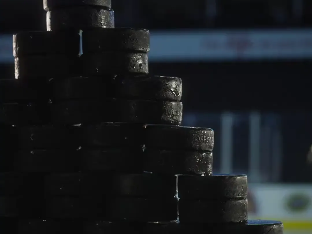 A pyramid of hockey pucks stacked on the boards of an empty arena
